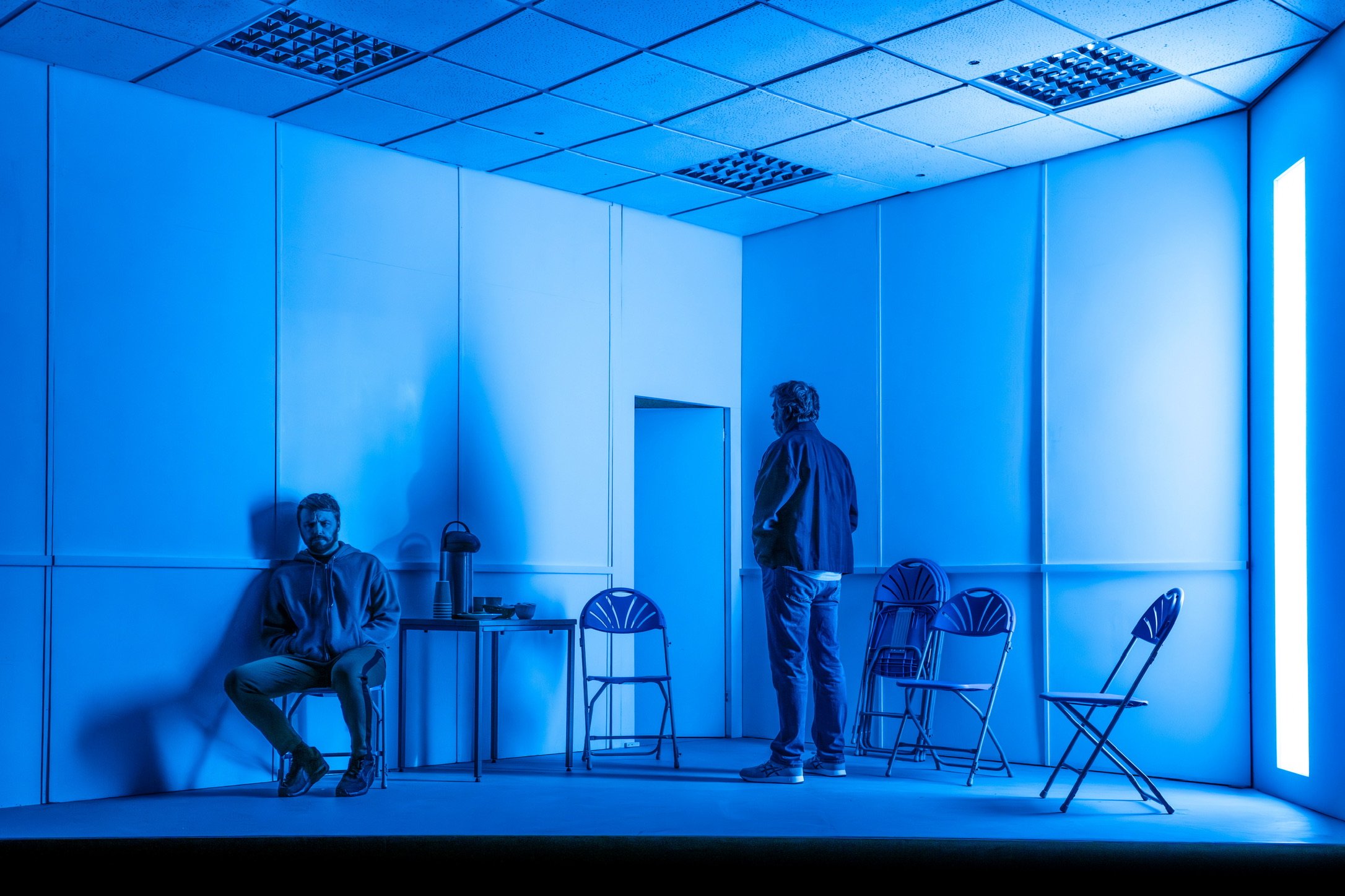 Two performers in the blue-lit room set of The Fifth Step.