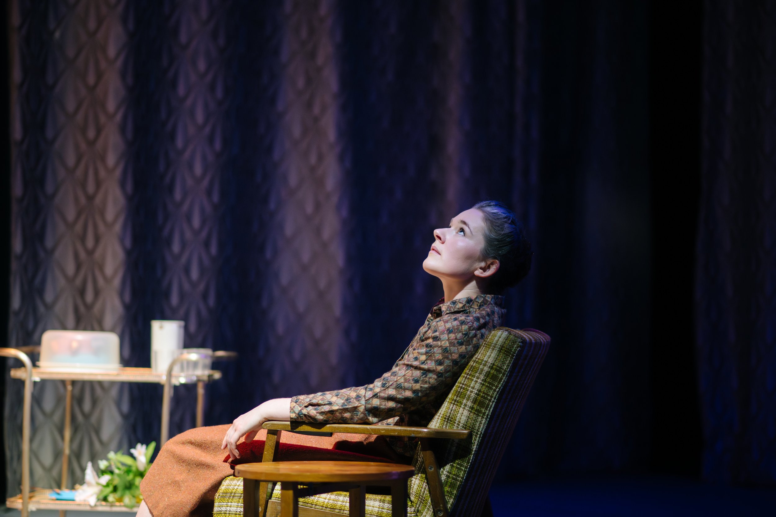 A performer seated beneath a patterned curtain in When Prophecy Fails.