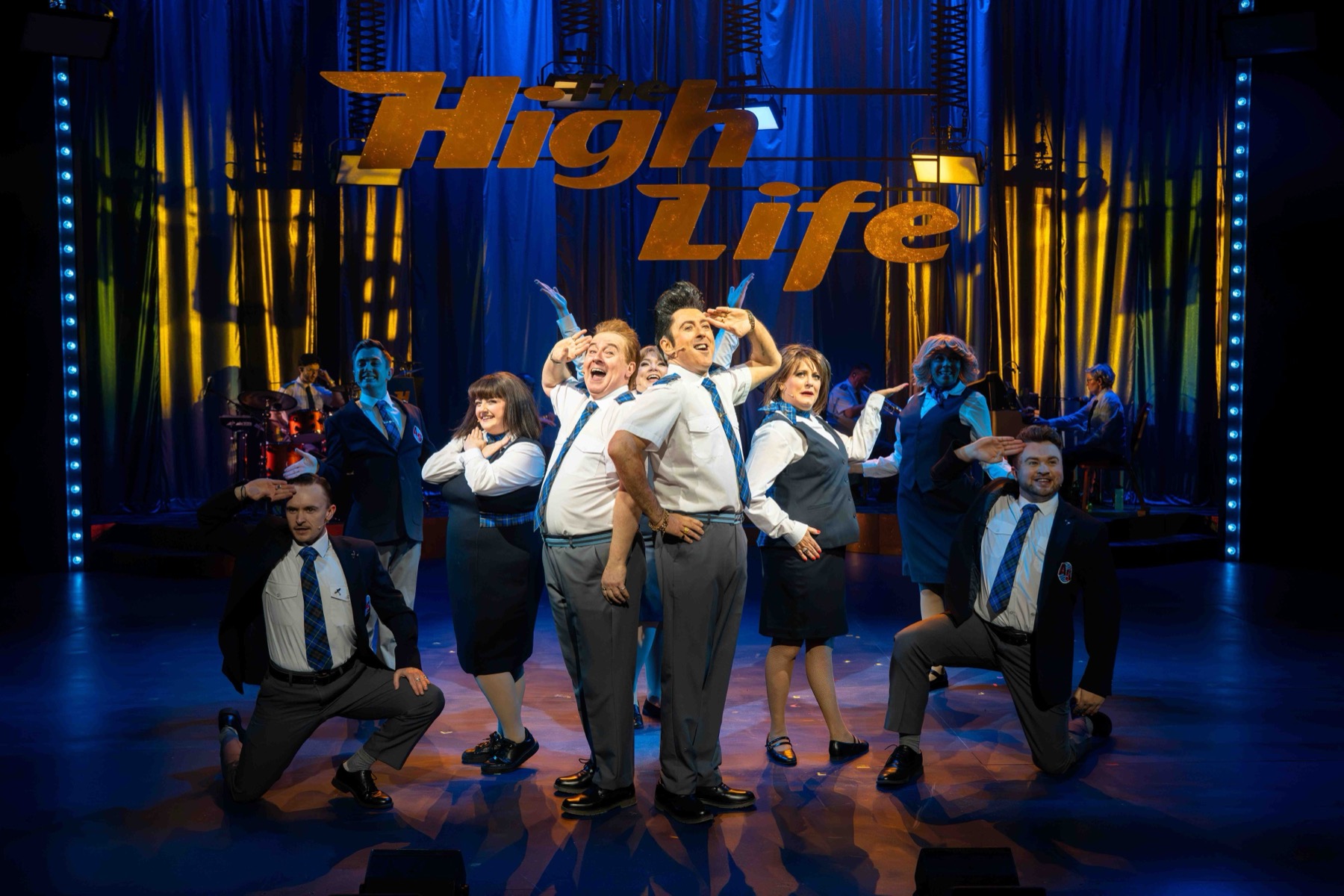The cast of The High Life on stage beneath the illuminated show title.